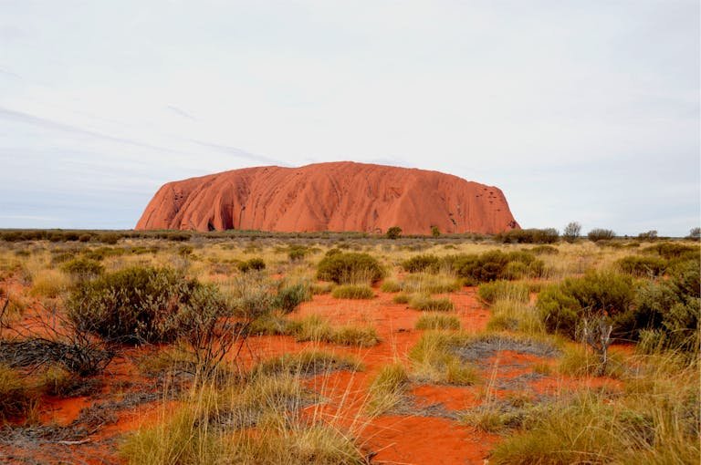 Scenic view of Uluru rock formation set in the arid Australian Outback landscape under cloudy skies.