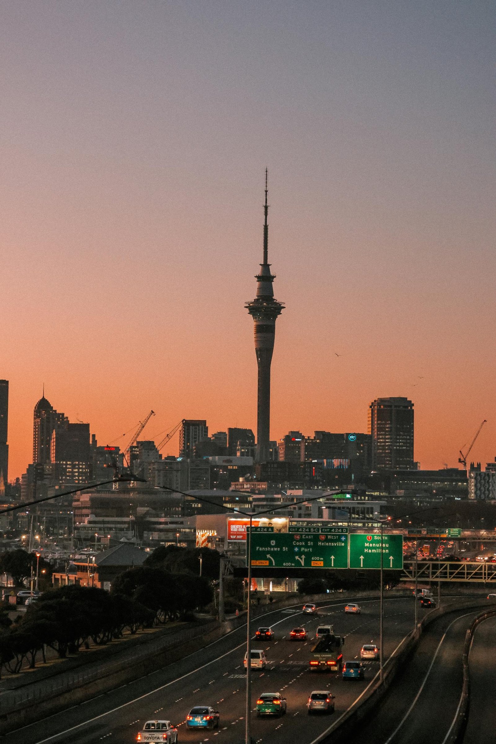 Beautiful view of Auckland skyline featuring Sky Tower at sunrise, highlighting city lights and traffic.