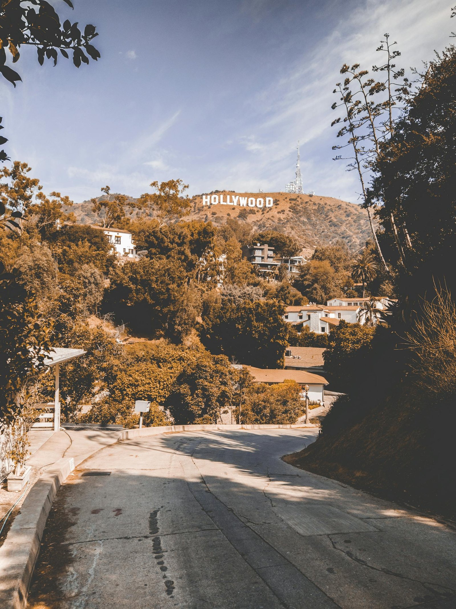 An empty winding road leading to the iconic Hollywood Sign in Los Angeles on a sunny day.
