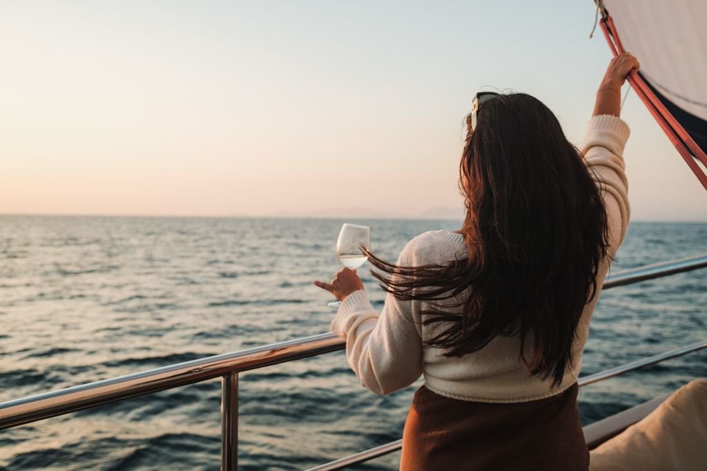 A woman with long brunette hair enjoys a drink while sailing at sunset.