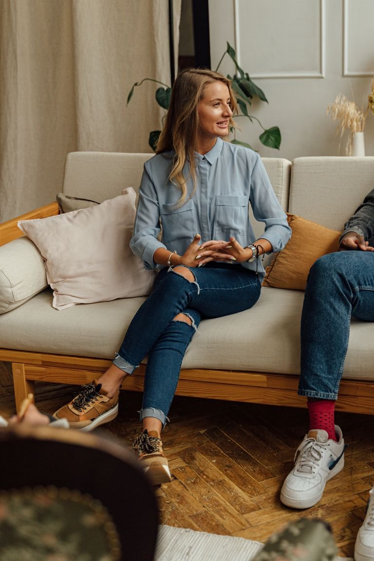 Caucasian woman seated on a sofa in a modern, stylish room, engaging in conversation.