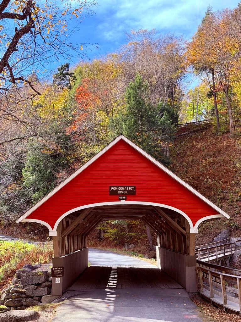 Red covered bridge in scenic autumn landscape with colorful foliage.